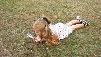 女孩用放大镜躺在草坪上。 一个女孩透过放大镜。 漂亮的女孩拿着放大镜。